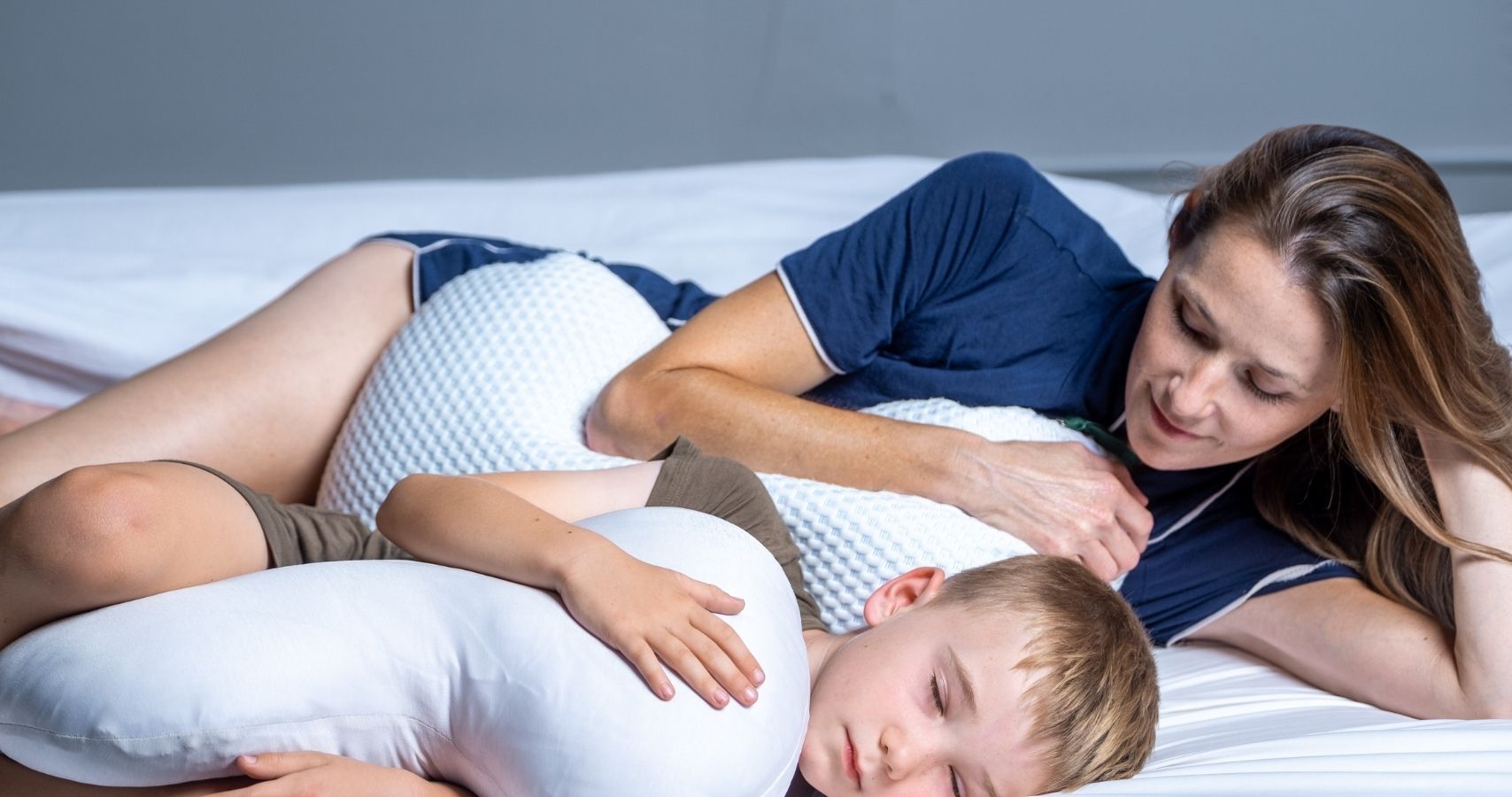 Woman and child lying on a bed with the Clutcher Therapeutic Pillow during rest time